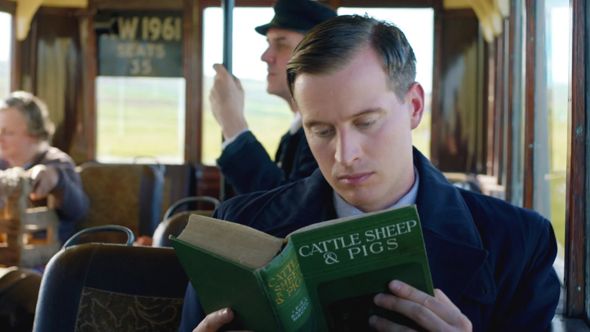 Color photo of actor Nicholas Ralph in his role as James Herriot, reading a book, in the TV series All Creatures Great and Small as seen on MASTERPIECE on PBS.