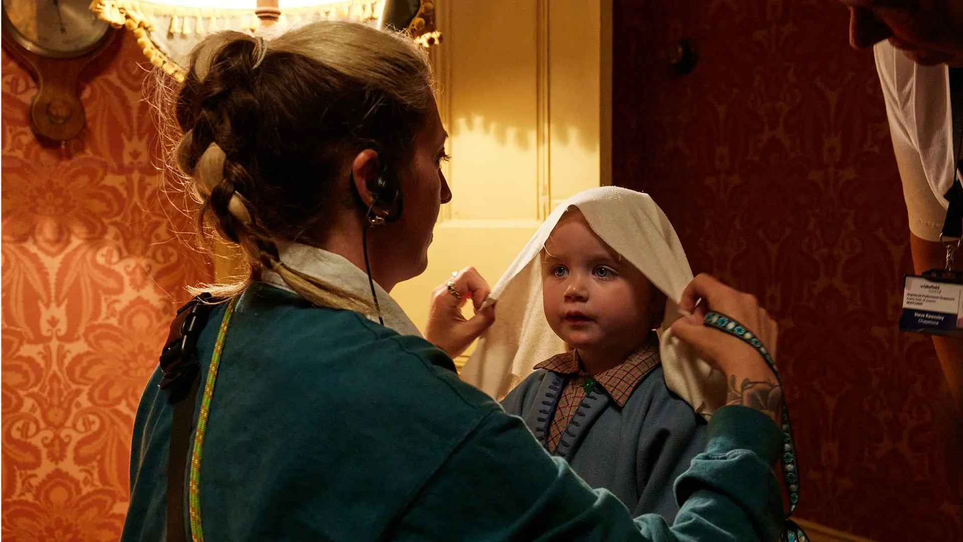 Autumn or Arlie Doyle, one of the two toddlers playing Rosie Herriot, stands still and sweetly while a crew member drapes a cloth over her head for her nativity play costume.
