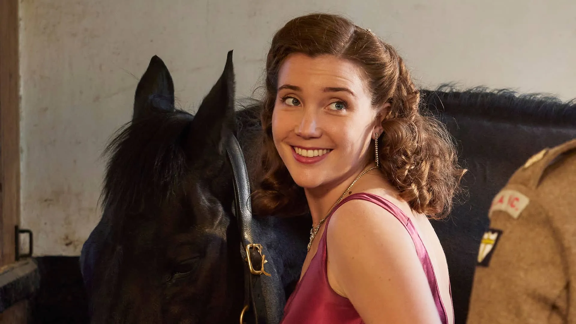 Standing next to her horse, Charlotte Beavoir (Gaia Wise) looks back over her shoulder at Tristan (off screen) with a lovely smile on her face