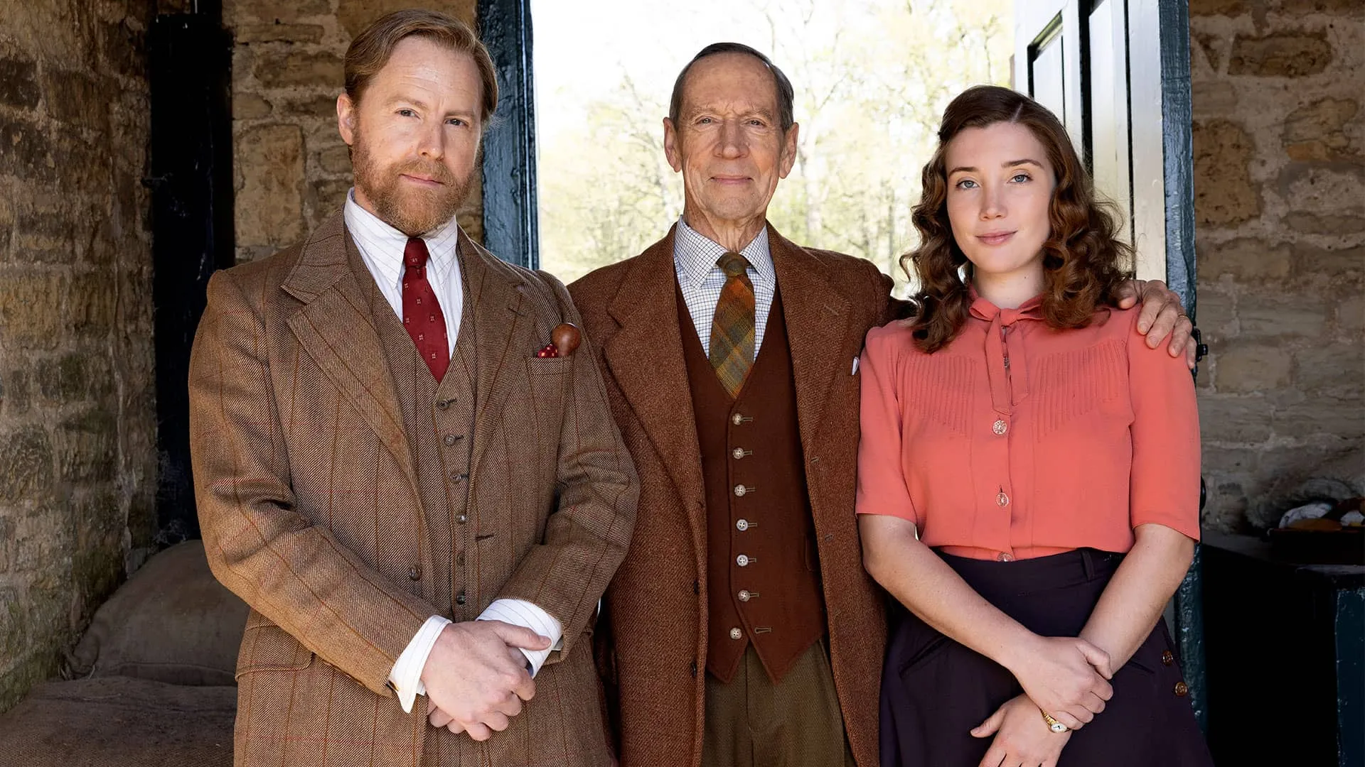 Samuel West as Siegfried Farnon, Jonathan Hyde as Captain Beauvoir, and Gaia Wise as Charlotte Beauvoir pose side-by-side in a barn