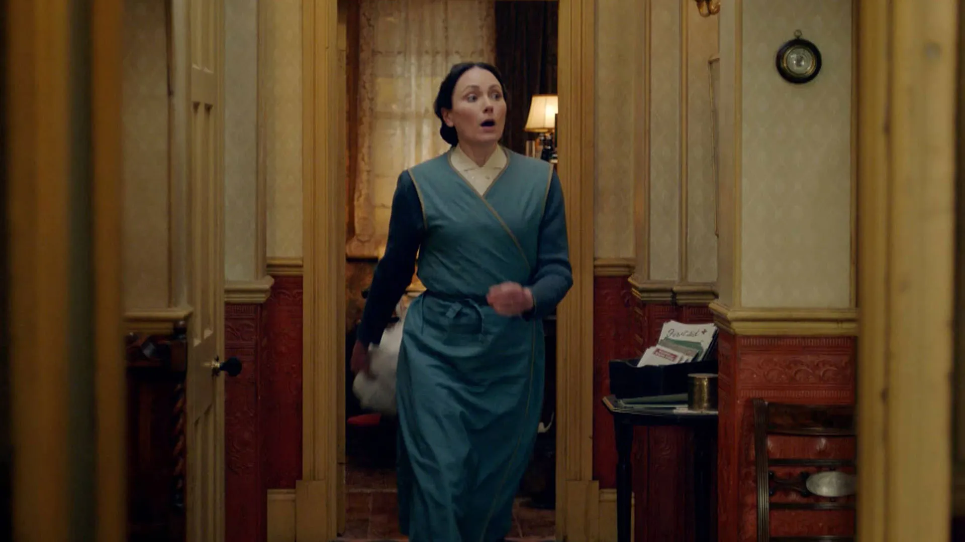 Mrs. Hall, looking frustrated, hurries down the hallway in search of Siegfried (off screen)