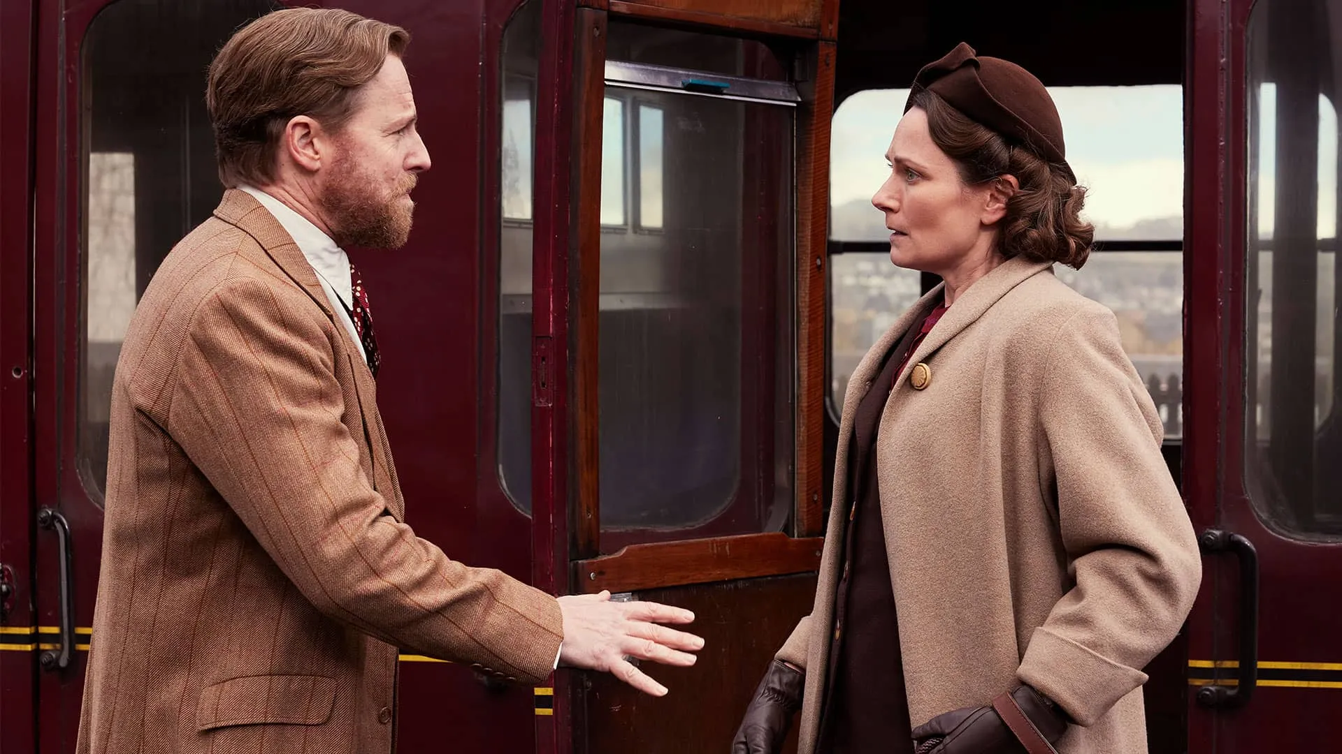 At the train station, Siegfried reaches his arm out urgently to Mrs. Hall, who looks at him with emotion on her face