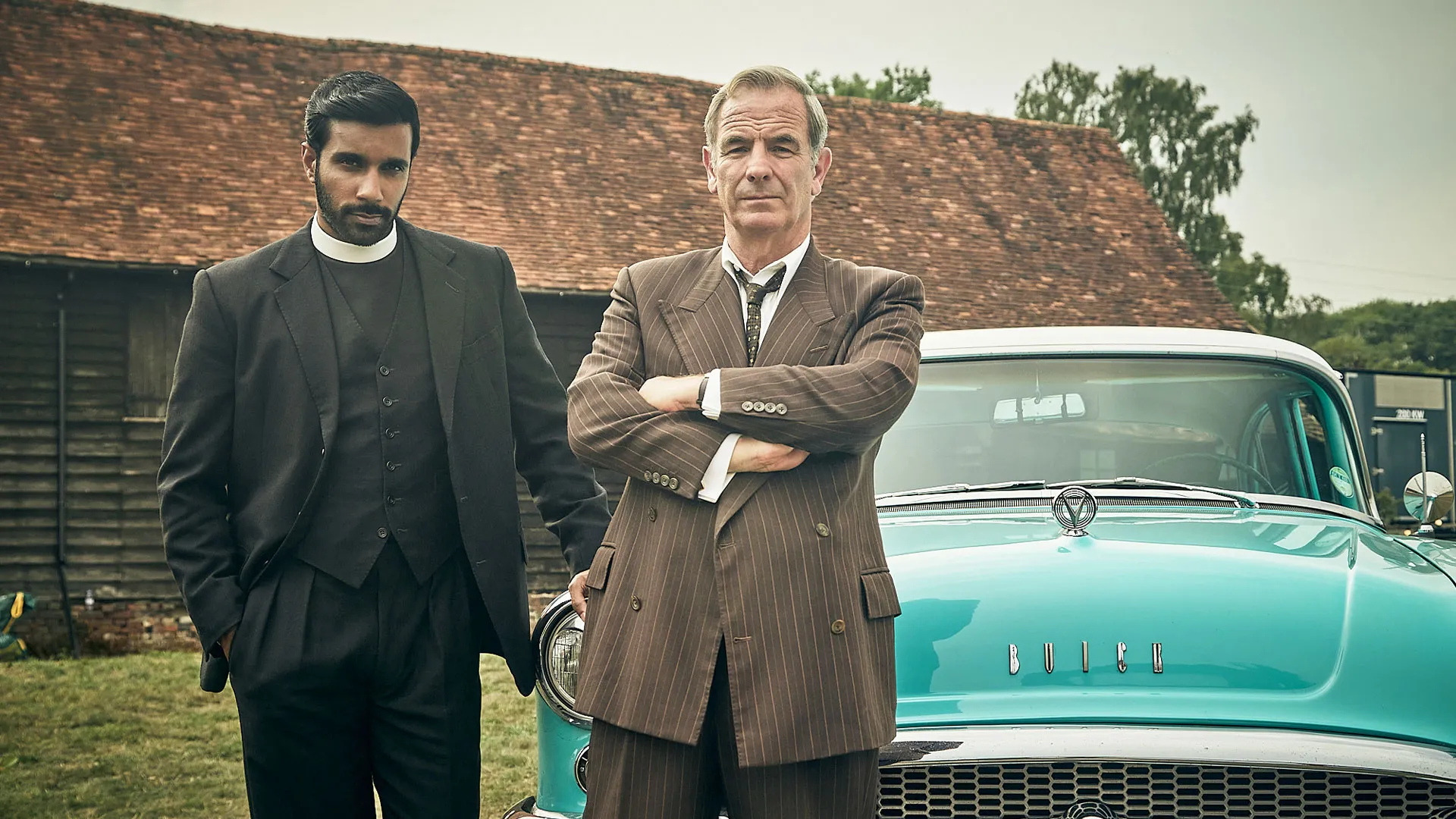 Rishi Nair as Alphy and Robson Green as Geordie posing by a car in Grantchester Season 11