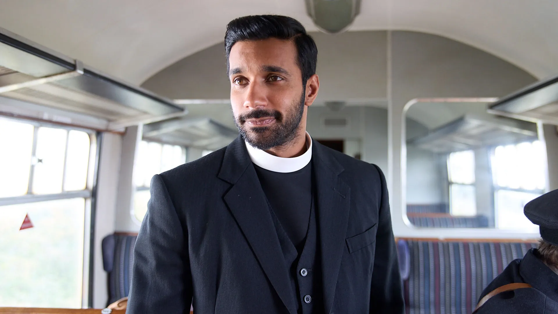 Rishi Nair as Alphy standing inside a train compartment in Grantchester Season 11