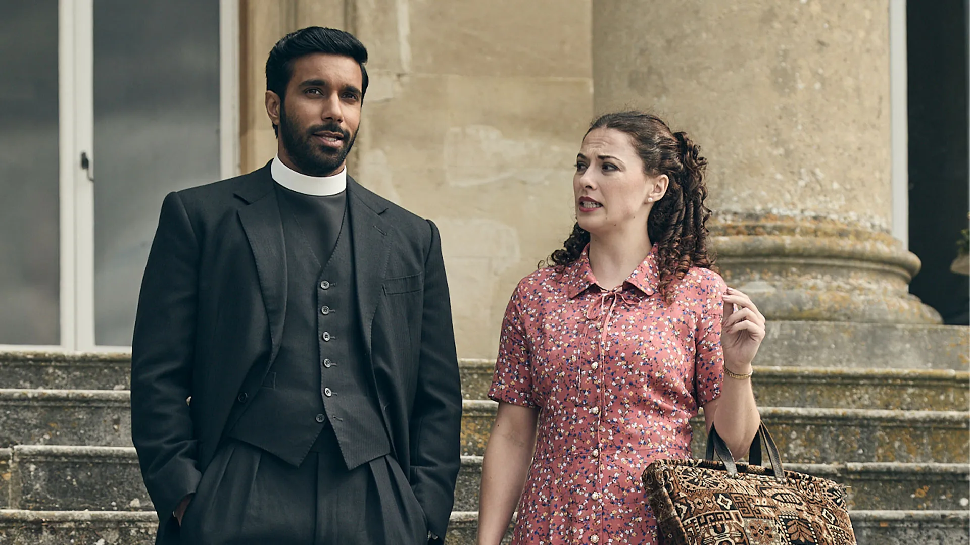 Rishi Nair as Alphy and Christie Russell-Brown as Meg standing together on steps in Grantchester Season 11