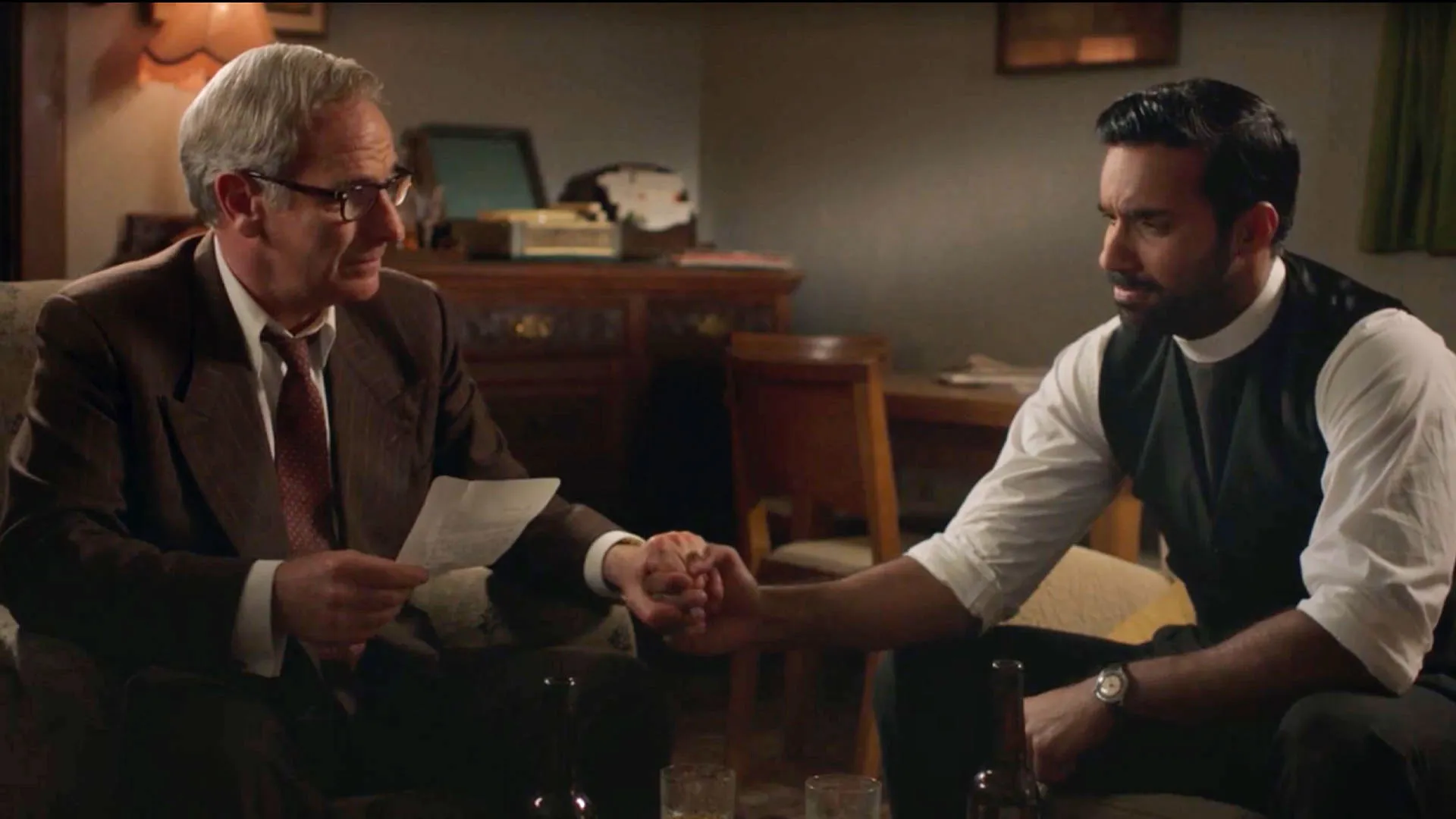 Robson Green as Geordie Keating and Rishi Nair as Alphy Kottaram sitting and holding hands in Grantchester Season 10