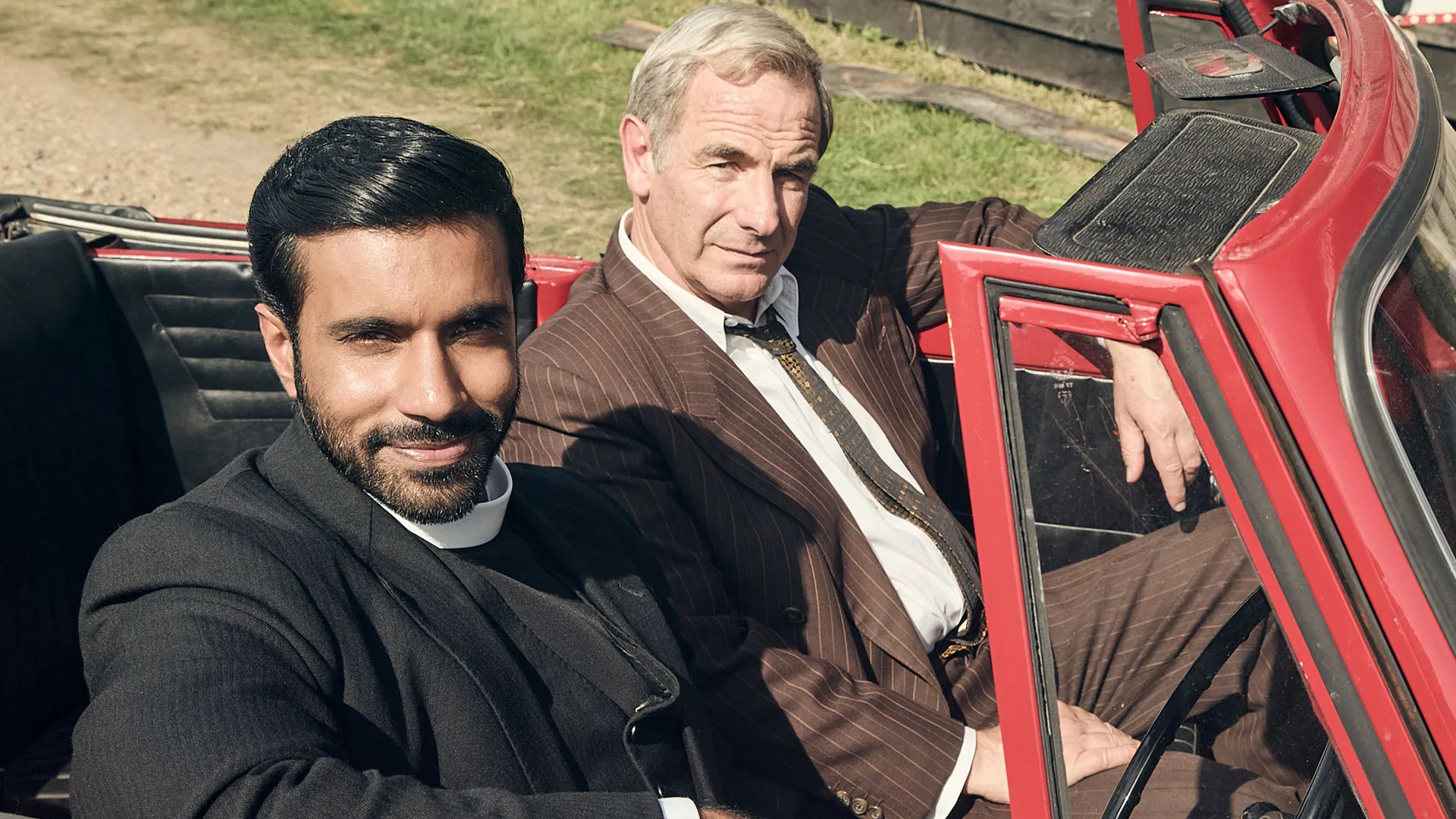 Rishi Nair as Alphy and Robson Green as Geordie sitting in a red car together in Grantchester Season 11