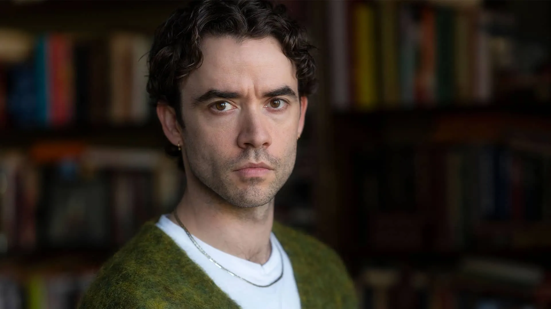 A serious Eliot Crace (Jamie Blackley) stands in front of a wall of books in Marble Hall Murders