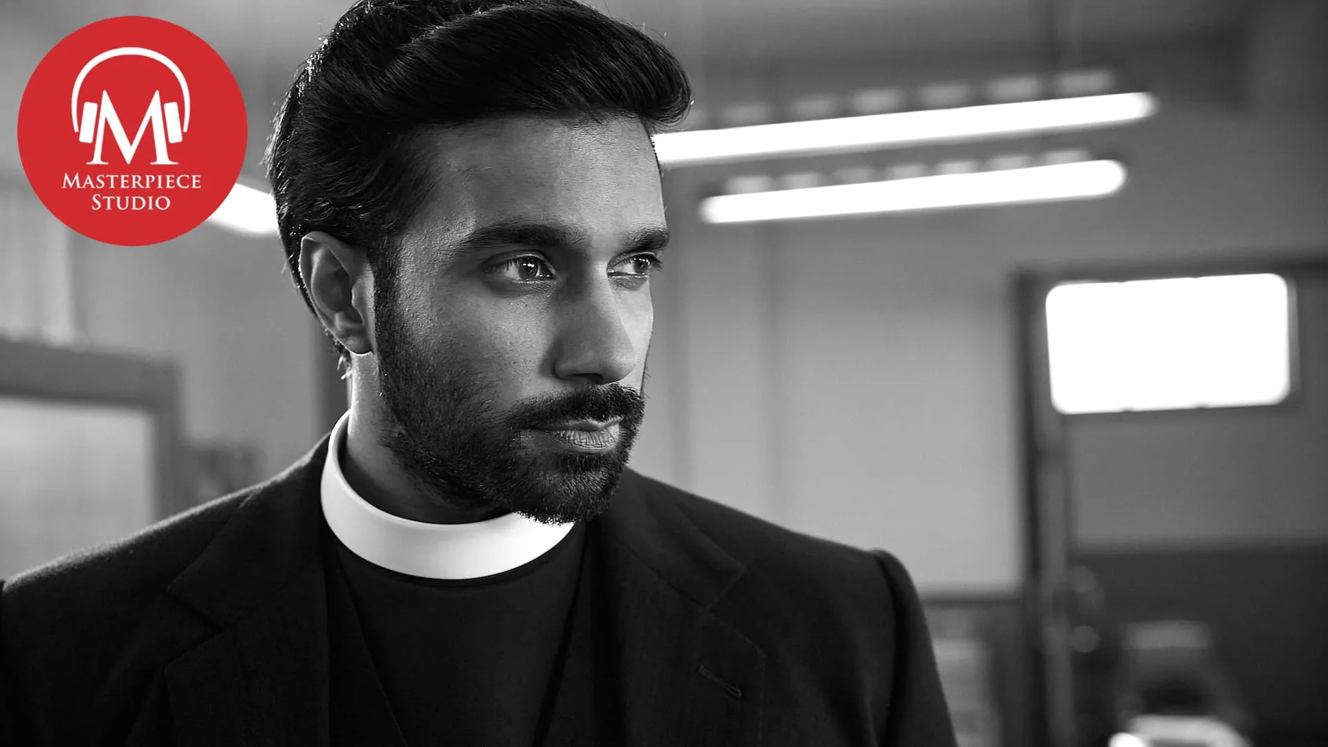 black and white photo of actor rishi nair as reverend alphy kottaram in grantchester with the red masterpiece studio logo in the top left corner
