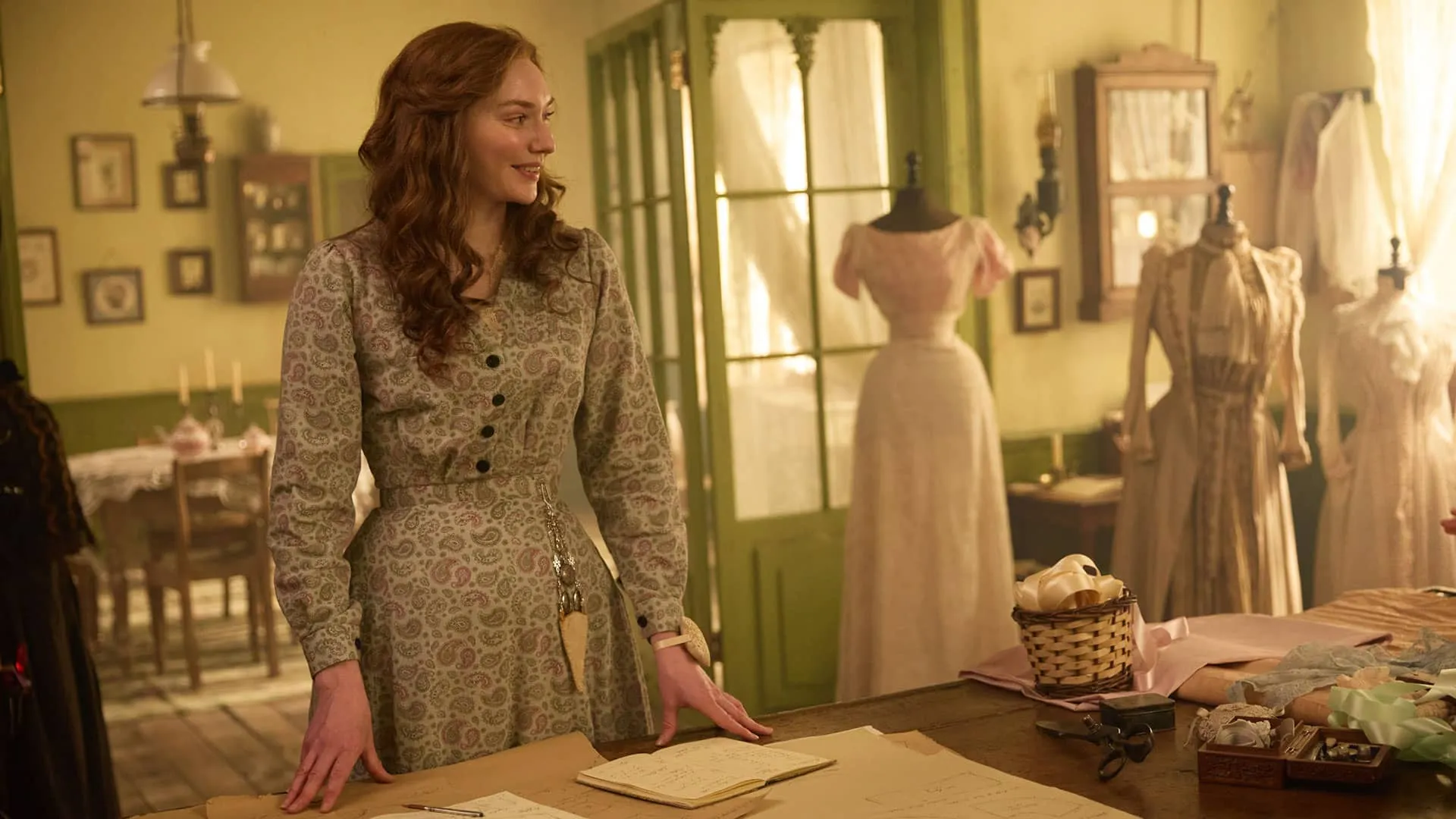 The Forsytes character Louisa standing in front of a work table in her dressmaker shop, with dress forms in the background