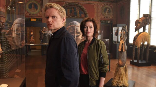 Marc Warren and Maimie McCoy standing in a gallery in Van der Valk Season 3
