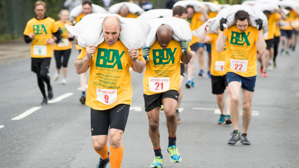 Photo of men carry bags of coal as they compete in the World Coal Carrying Championships in Gawthorpe, Yorkshire.