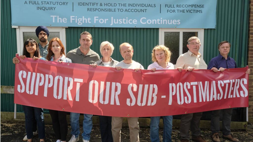 Alan Bates and other Subpostmasters and spouses stand outdoors, defiantly holding a banner saying 