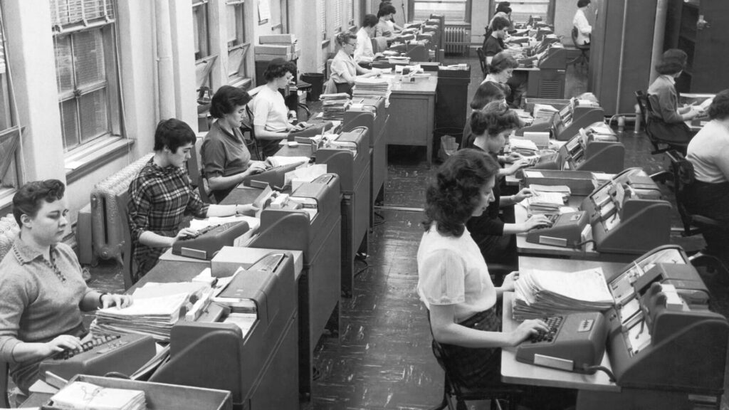 Archival photo of over a dozen female office workers entering data using tabulating machines and punch cards, 1958.