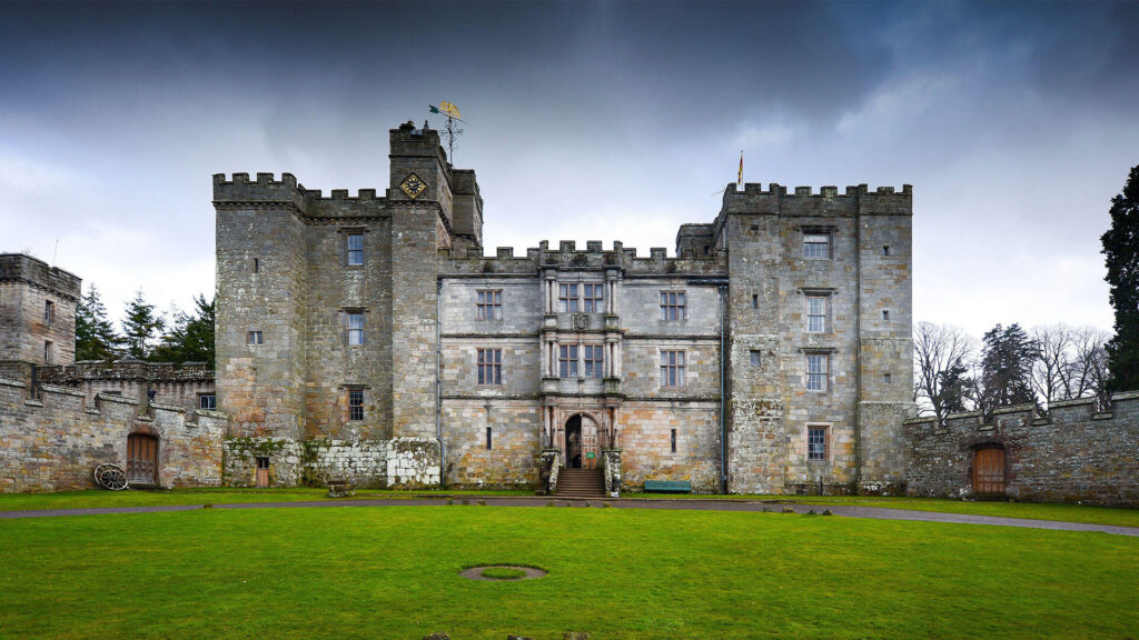 The stone exterior of the medieval Chillingham Castle on a gloomy day with dark clouds in Northumberland, England.