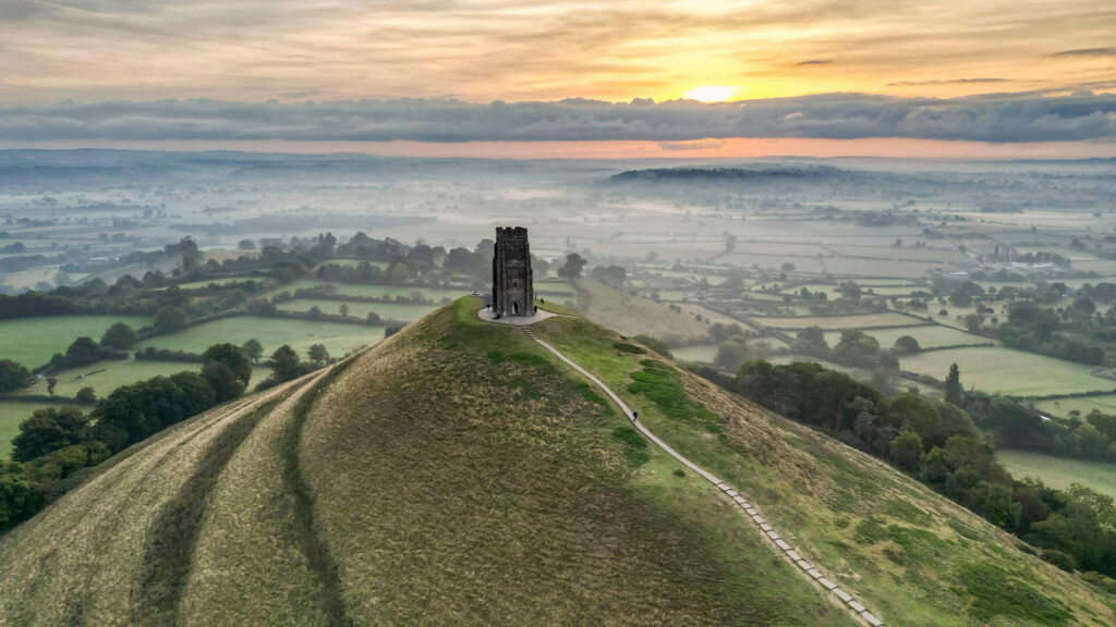 Color photo of the 500 foot Glastonbury Tor (or hill) at sunset, with ancient St. Michael's tower sitting at the crest in Glastonbury, England..