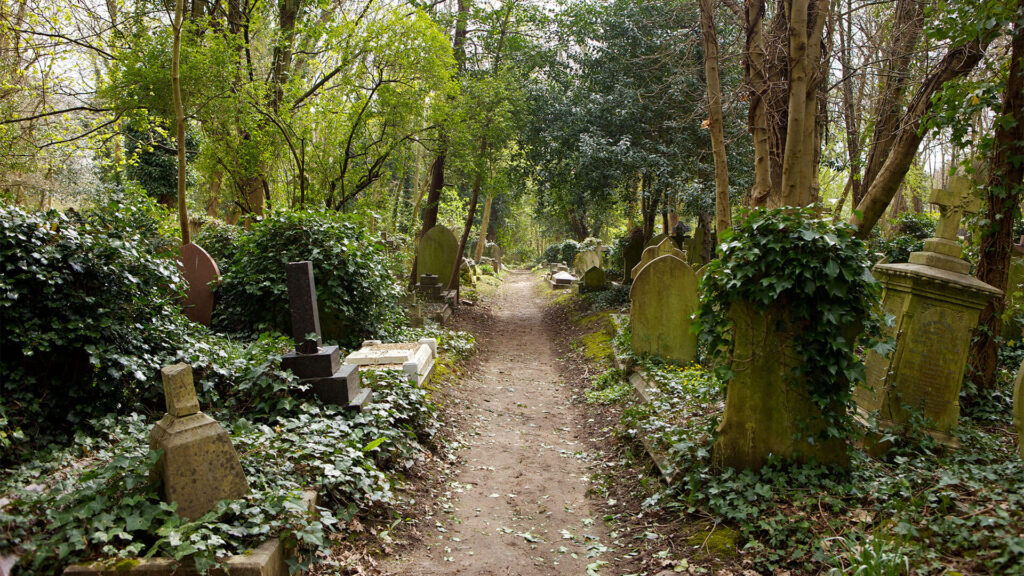 Color photo of a dirt path among tilted gravestones in the Victorian-era Highgate Cemetery, London.