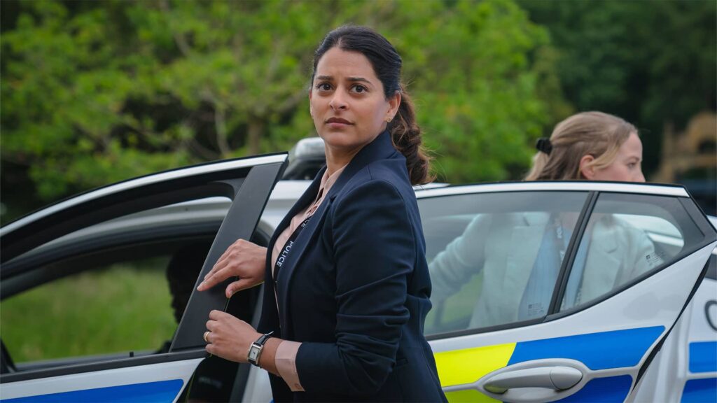 Standing outside of her squad car, DCI Tanika Malik stares intensely at something in the distance