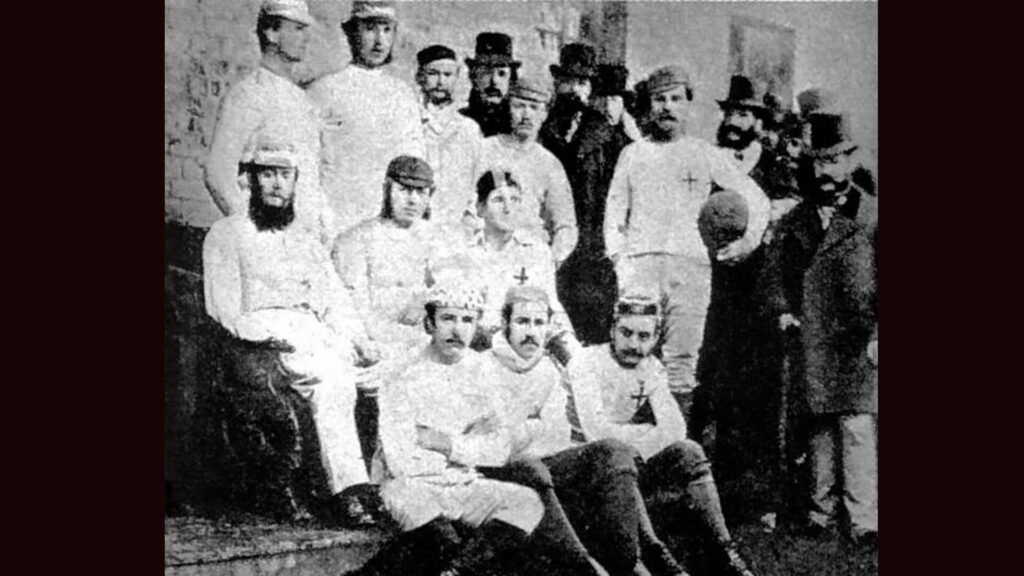 A black and white archival photo of Sheffield Football Club UK, 1857 with three rows of players dressed in white with caps.