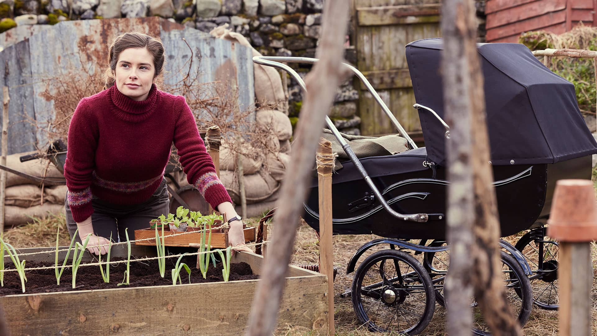 Helen Herriot kneeling at a raised bed in a victory garden, looking contemplative.
