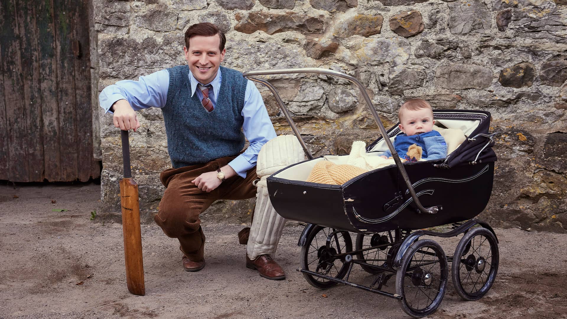James Herriot crouching with cricket bat next to the pram with baby Jimmy peeking out