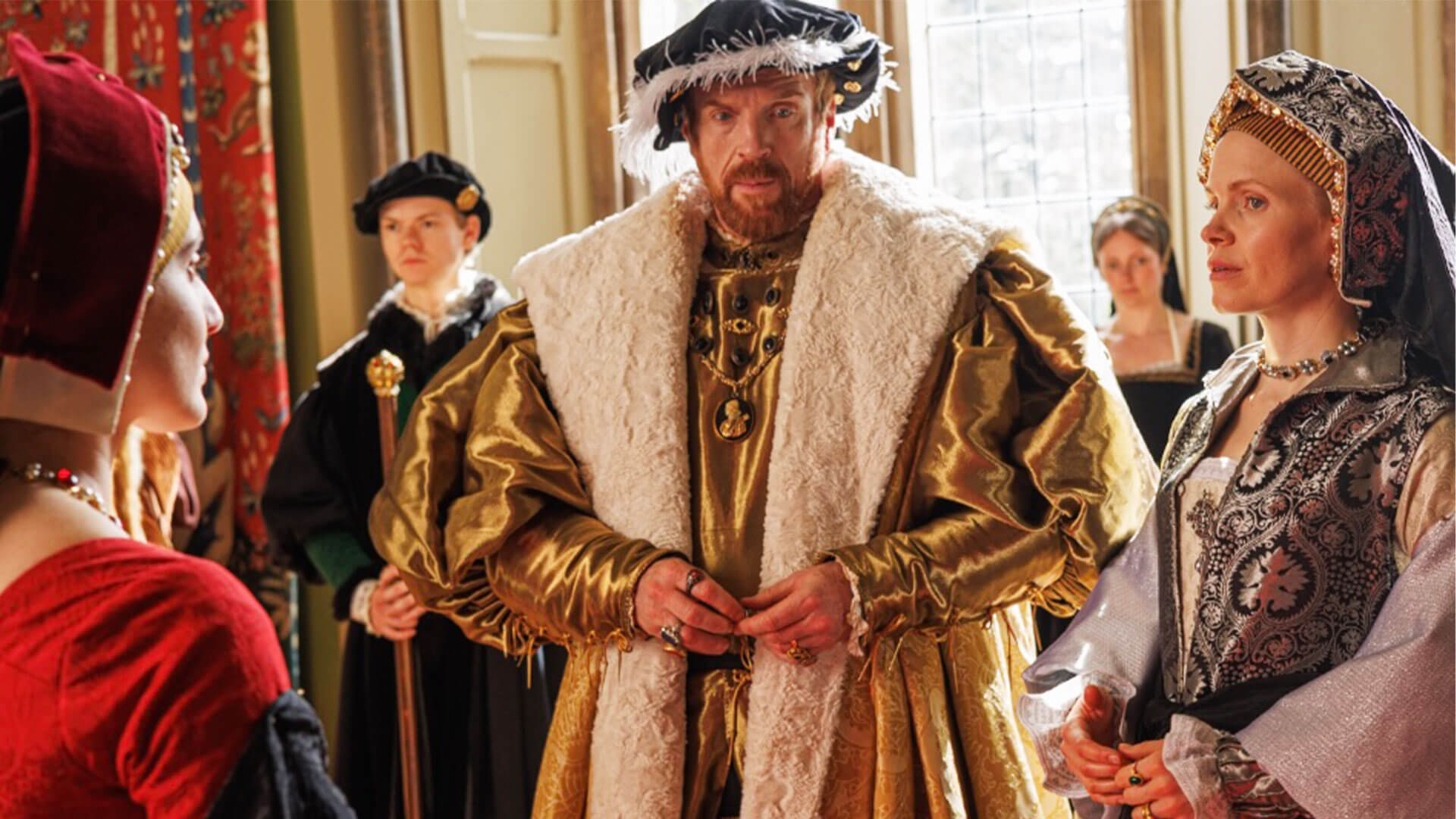 Actors Lilit Lesser in costume as Princess Mary (far left), Damian Lewis as Henry VIII (center) and Kate Phillips as Jane Seymour in PBS MASTERPIECE's Wolf Hall: The Mirror and the Light.