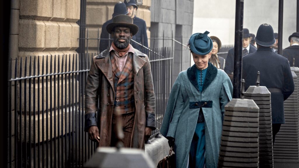 Color image of a scene from Miss Scarlet Season 6 on MASTERPIECE on PBS. Actor Ansu Kabia as Moses Valentine walks beside Kate Phillips as Eliza Scarlet.