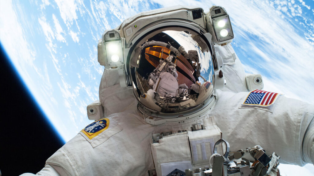 Photo of the front of an astronaut in a spacesuit doing a space walk with Earth in the background.