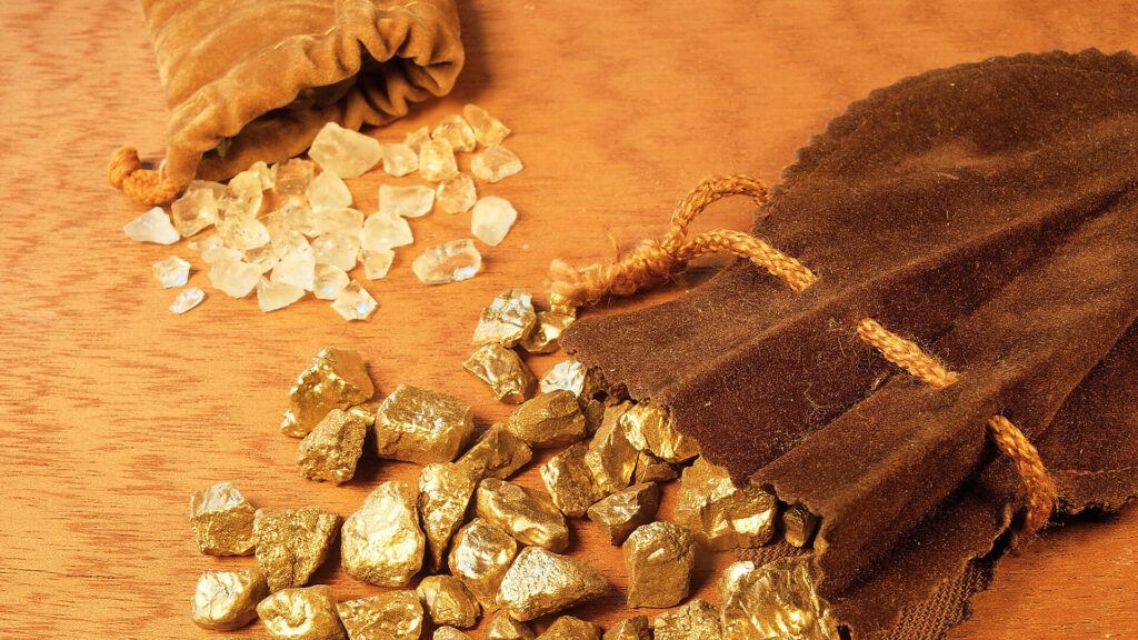 Color photo showing an open sack of raw diamonds next to an open sack of gold ingots.