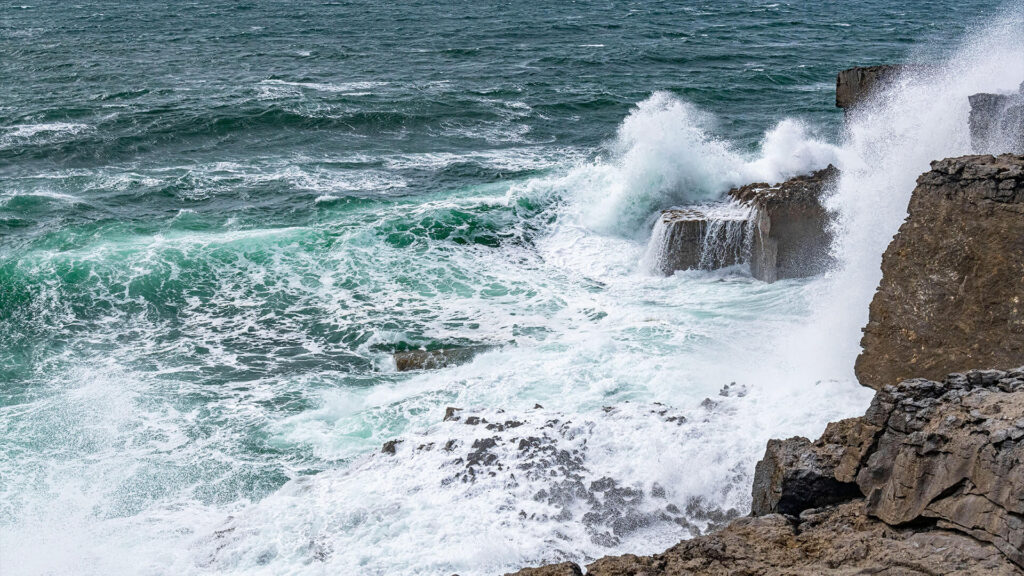 Color photo of a blue ocean's waves crashing on a rocky shorelinee.