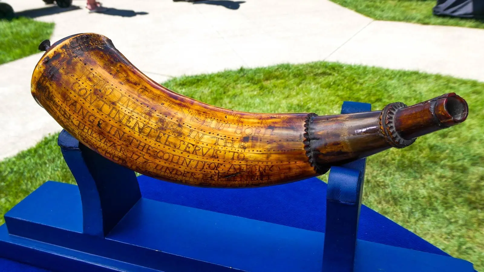 A close up of a wooden powder horn on a Table with dark brown etchings of words.