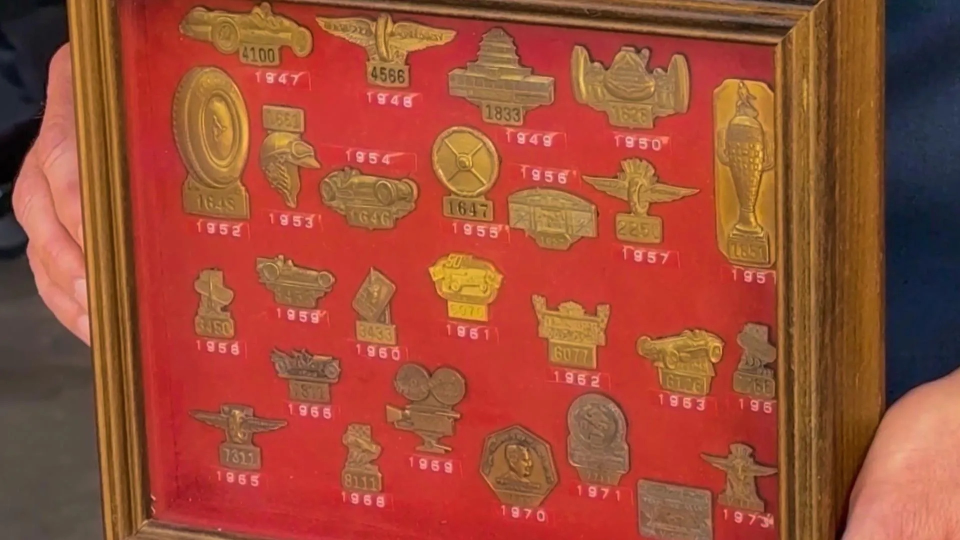 A plaque of golden car themed pins mounted on a red background. Beneath each pin is its respective year written in white.