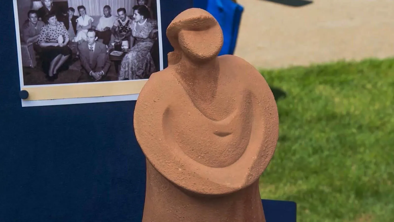 A terracotta figure that resembles a woman's sillouhette sits on a table next to a black and white family photo.