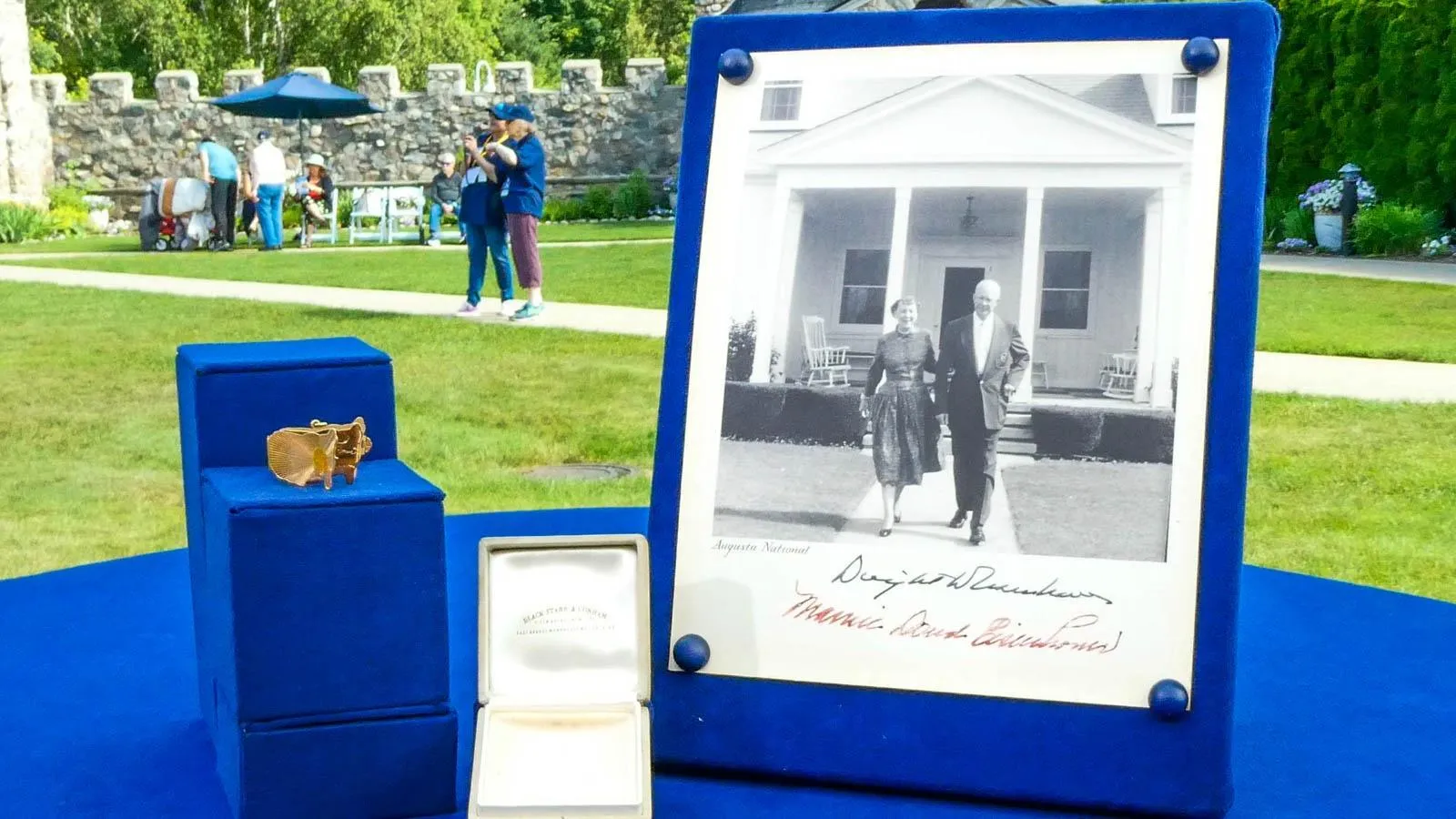 A locket is placed on a blue display stand next to an open box and mounted black and white photo of president Eisenhower.