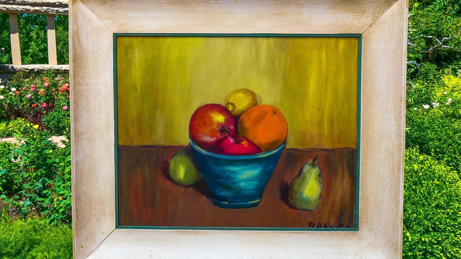 A paint of a fruit in a teal bowl on a brown table encased in a wooden frame.