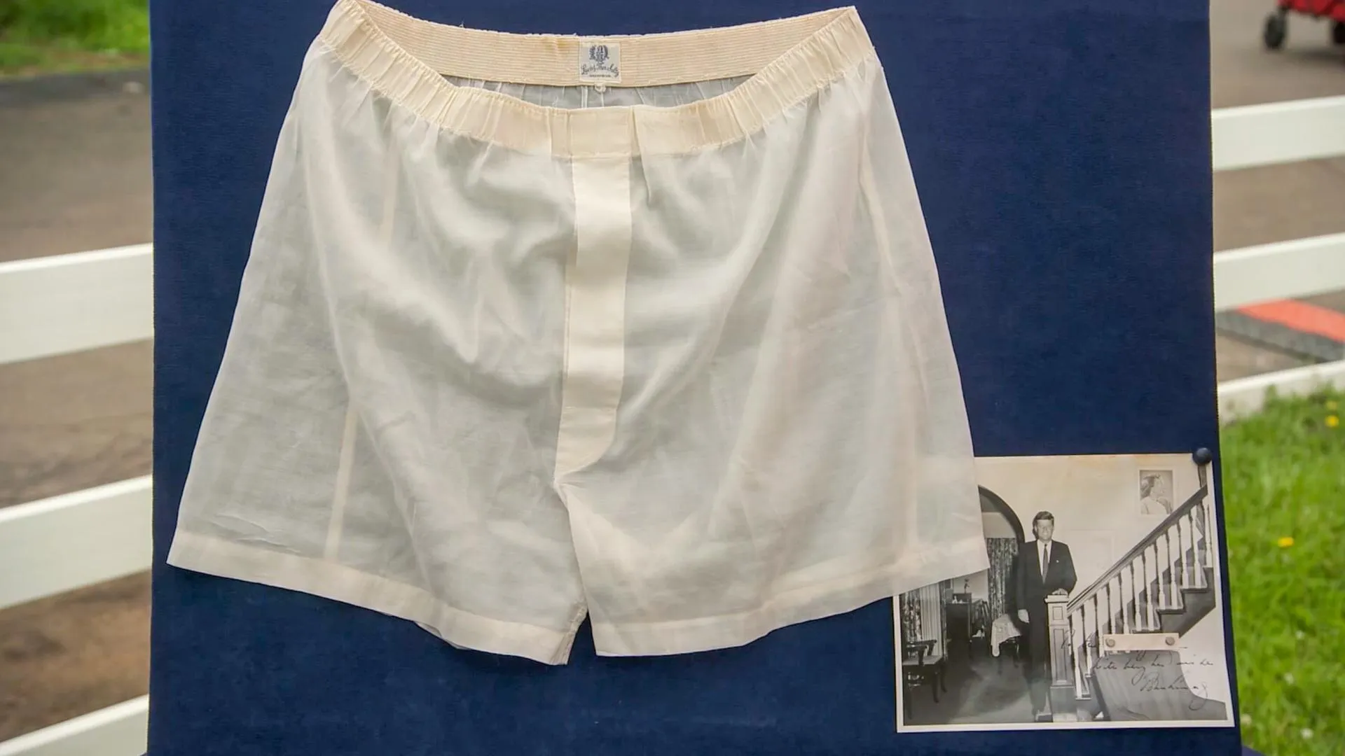 A pair pf white silk boxers mounted on a blue foam board next to a black and white photo.