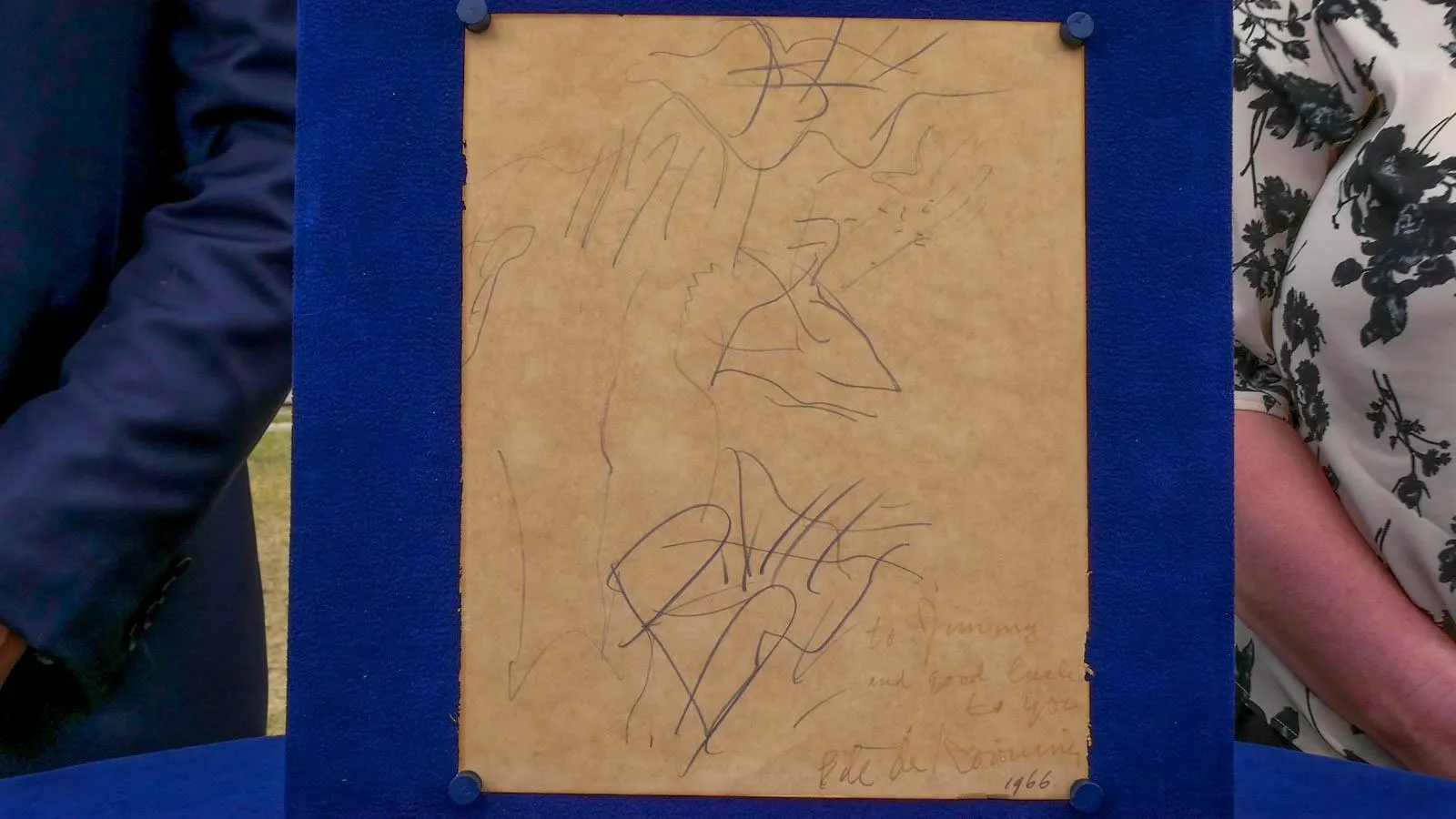 A brown piece of parchment mounted on a blue foam board with black scribbles on it dated to 1966.