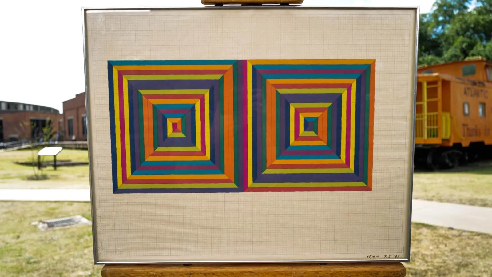 Two alternating multicolored squares printed next to each other on a grid background on an easel against an outdoor backdrop.