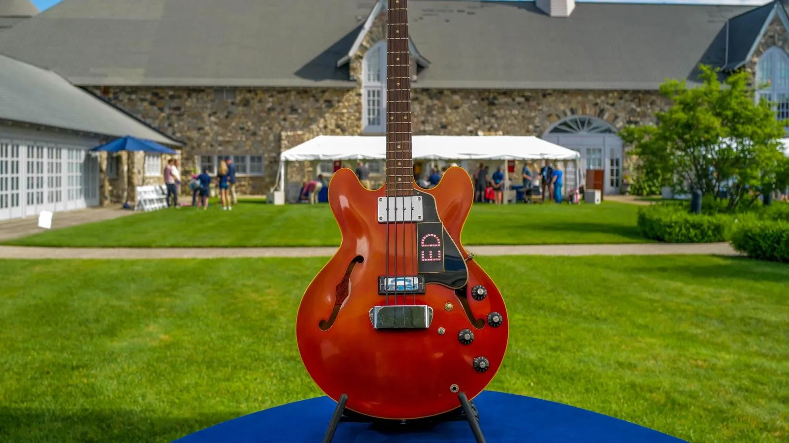 A guitar of shiny orange wood with the name ED bedazzled on it is mounted on a blue table for display.