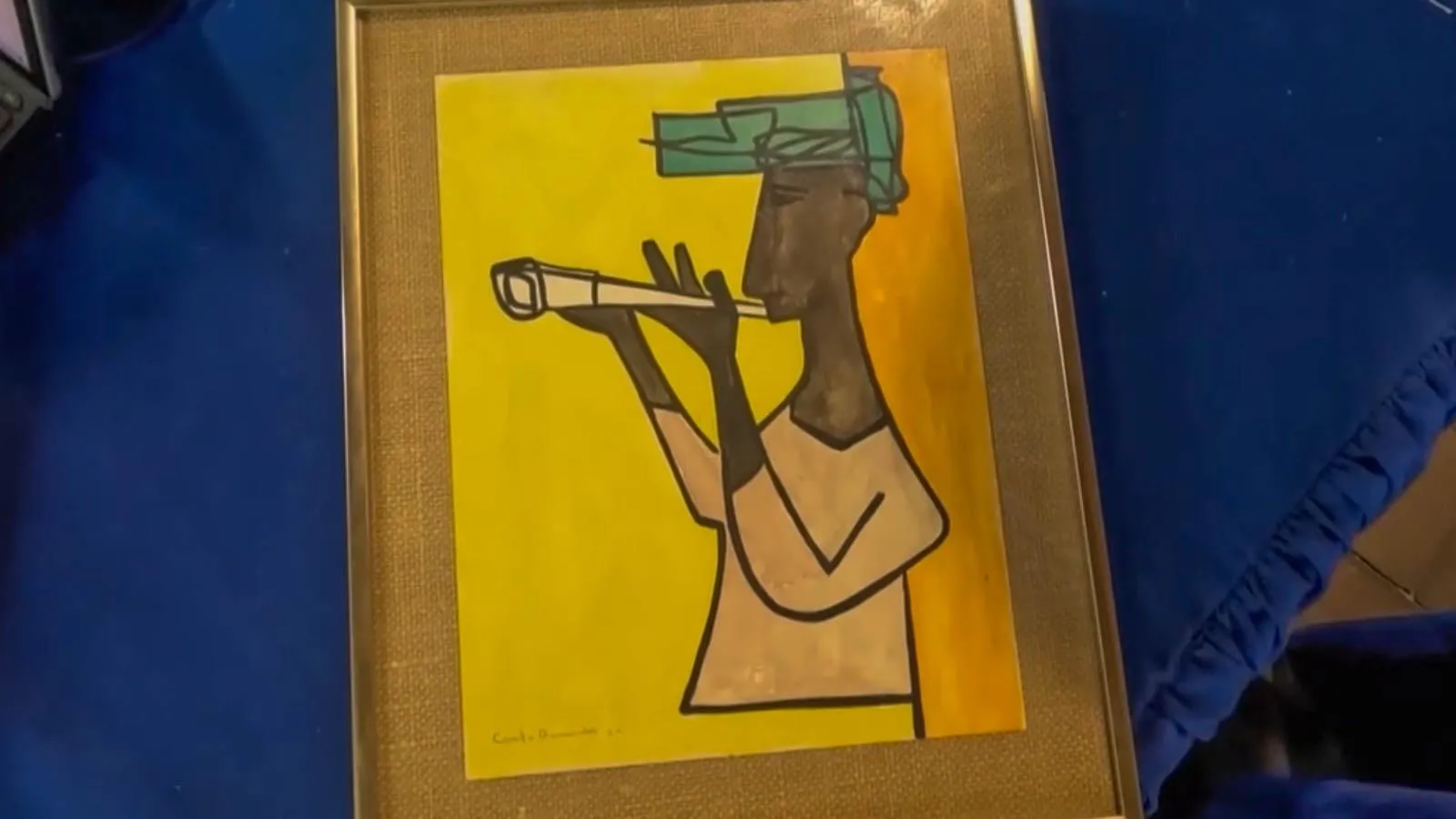 Close up of a framed watercolor of a man playing an instrument in a green hat against a yellow background in a cubist art style.