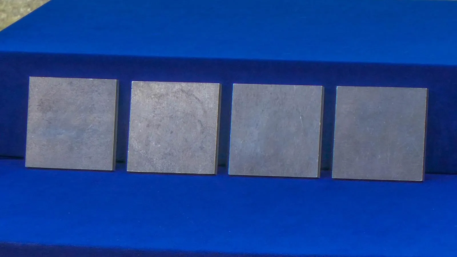 Four squares of aluminum displayed against a royal blue background.