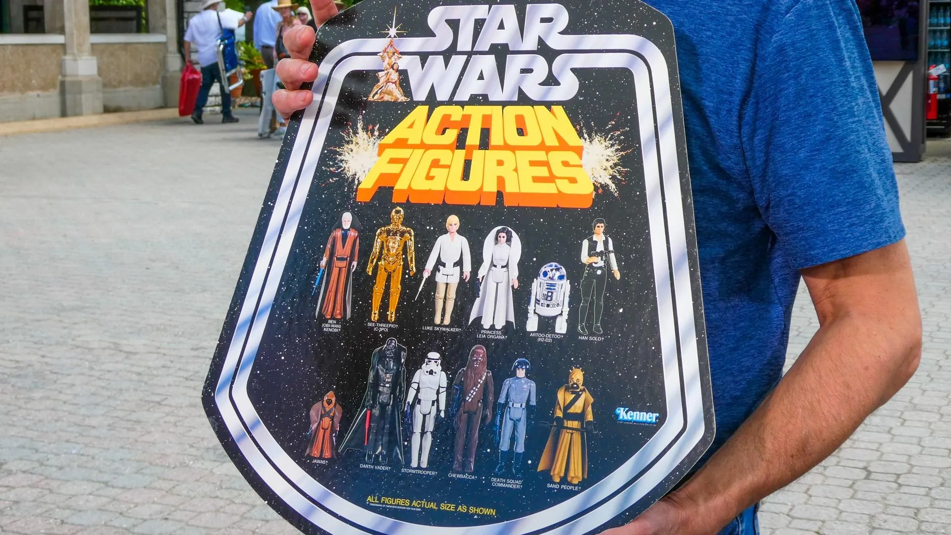 A person in a blue shirt holds a display board that says Star Wars Featuring all of the characters lined up in two rows.
