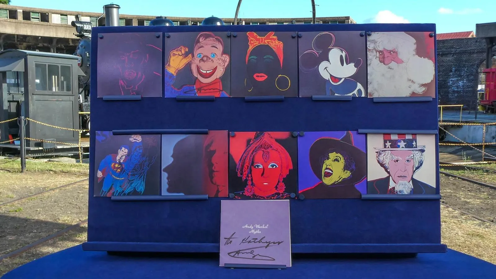 A series of pop culture paintings featuring the likes of Mickey Mouse, Superman, and Uncle Sam mounted on a blue board.