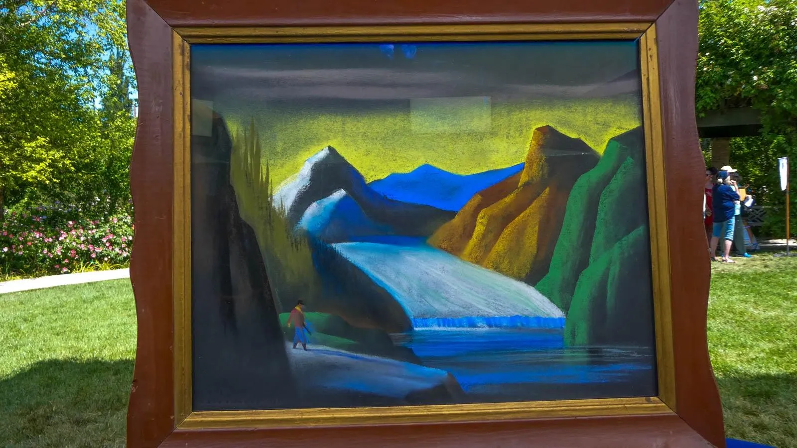 A landscape painting of a person walking in a winter scene in front of colorful mountains housed in a dark wooden frame.