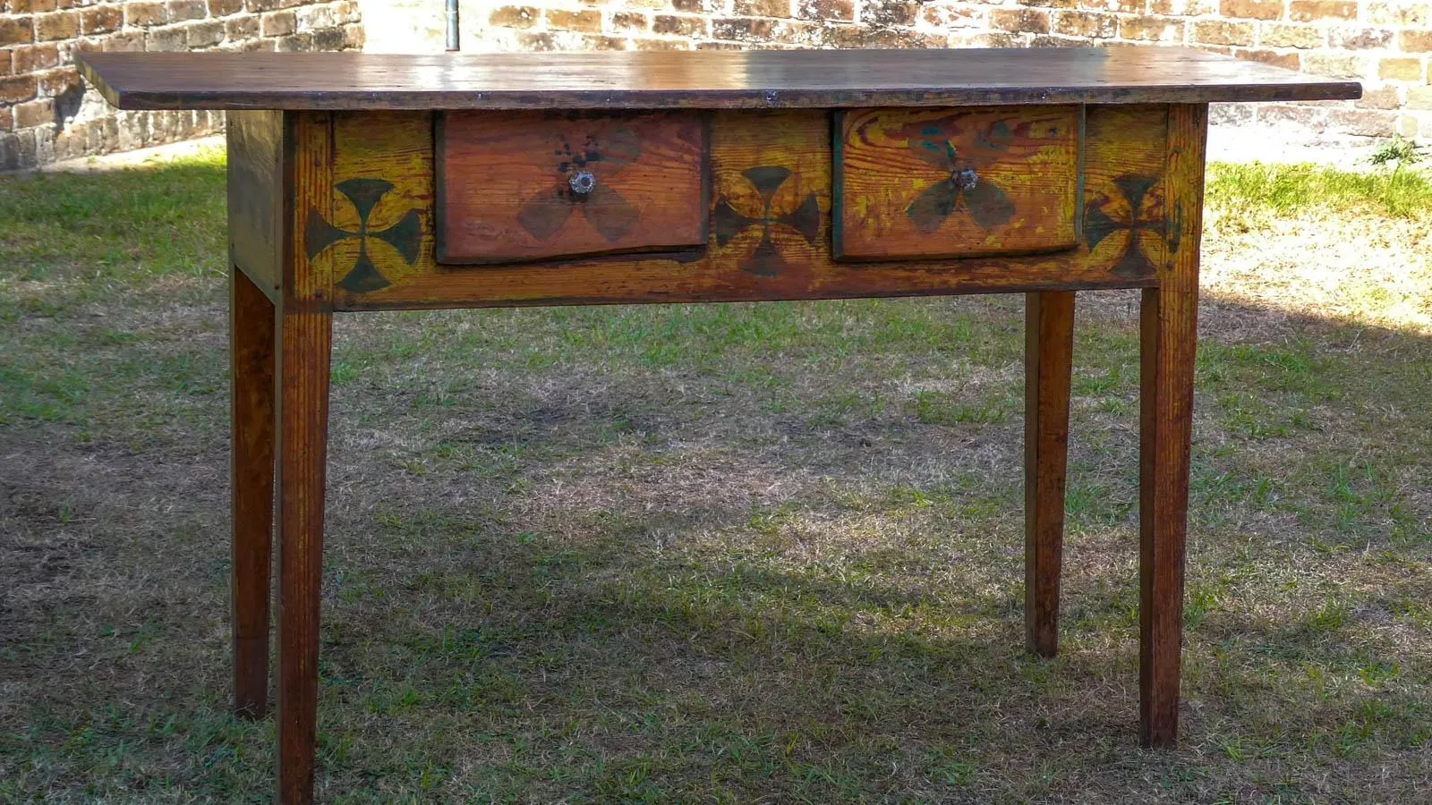 A rectangular table stands in the grass painted yellow with orange drawers.