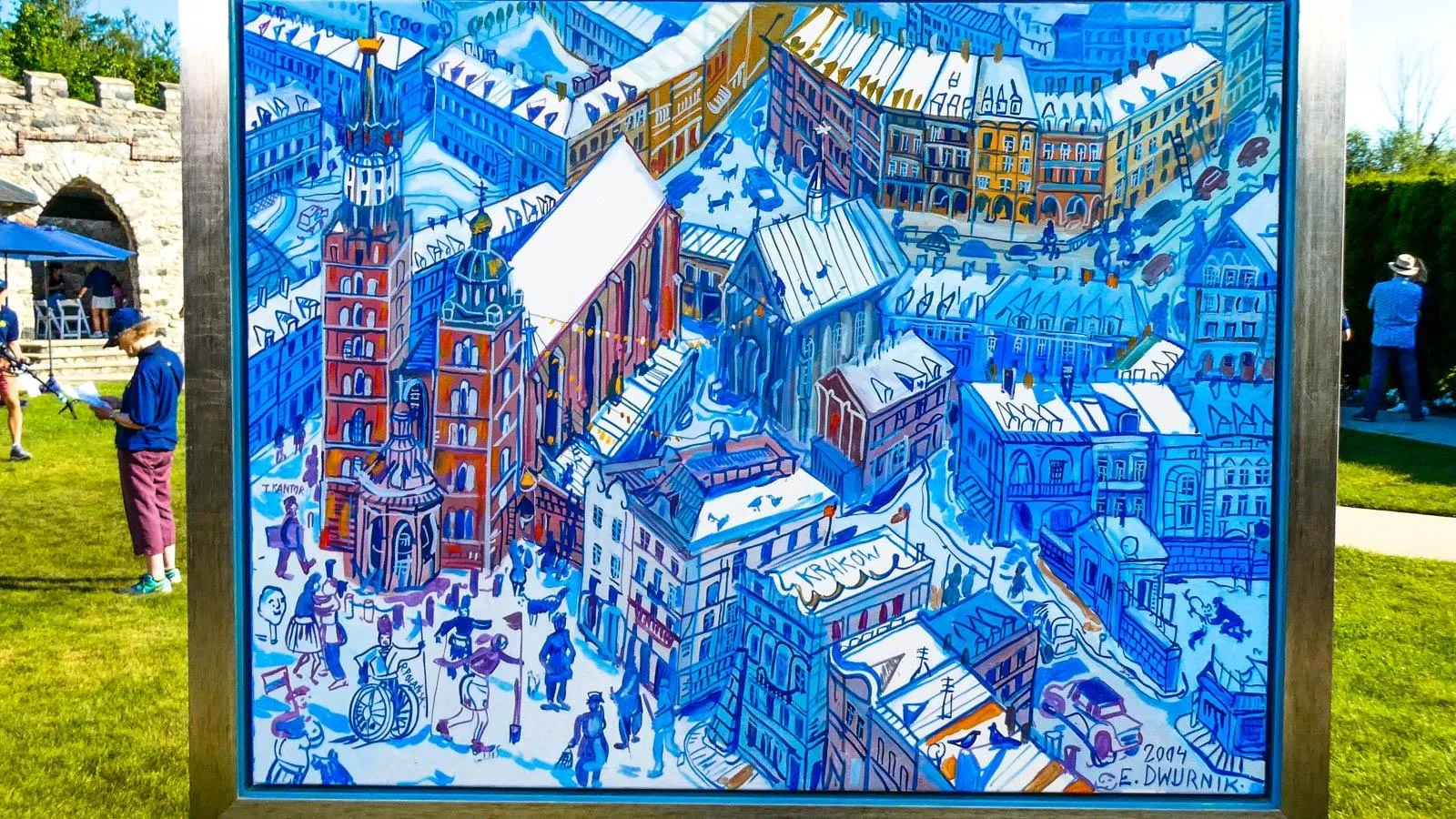 A blue and white colored scene cityscape of Kraków sits on an easel against an outdoor backdrop