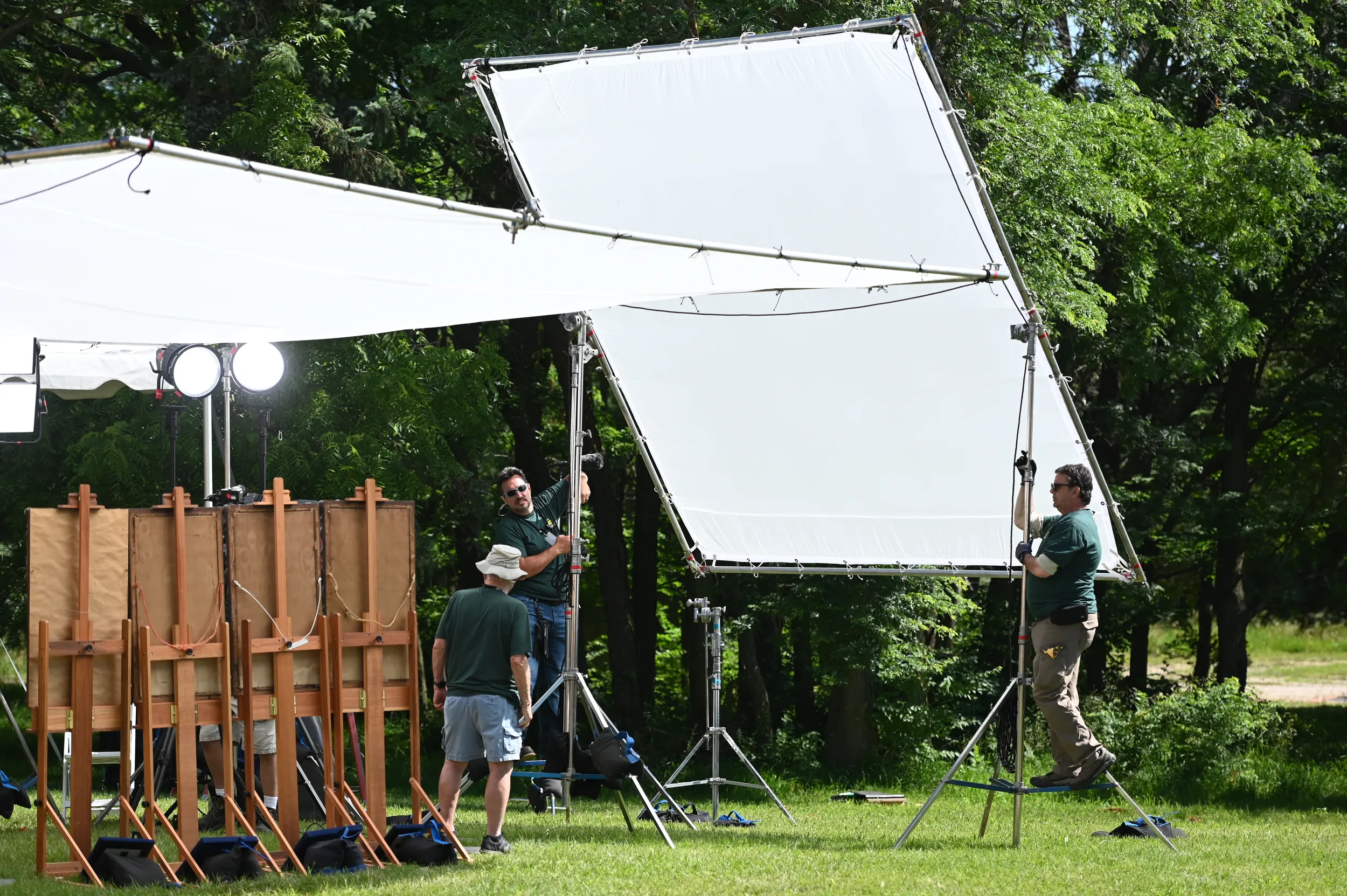 Three Roadshow crew members in dark green shirts rig up a white scrim that blocks the sun.
