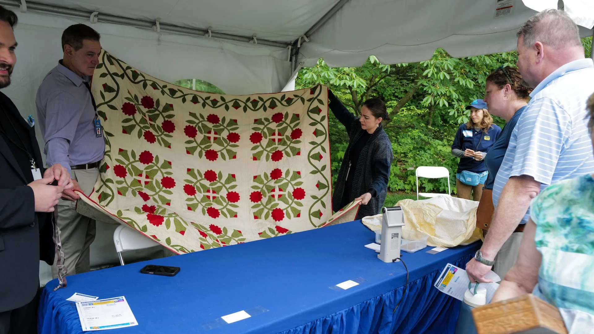 A photo of appraisers holding up a quilt with red flowers