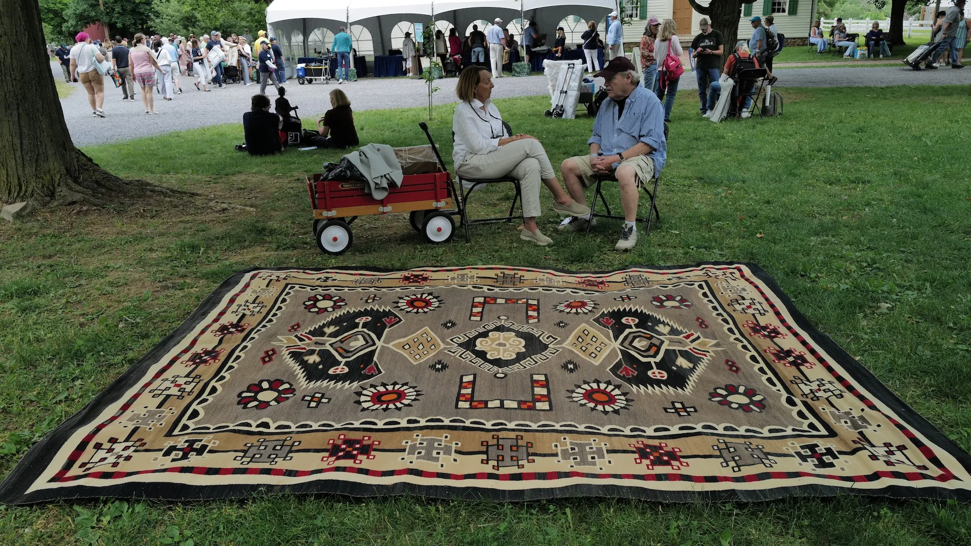 A photo of two guests sitting down by a large rug laid out on the grass