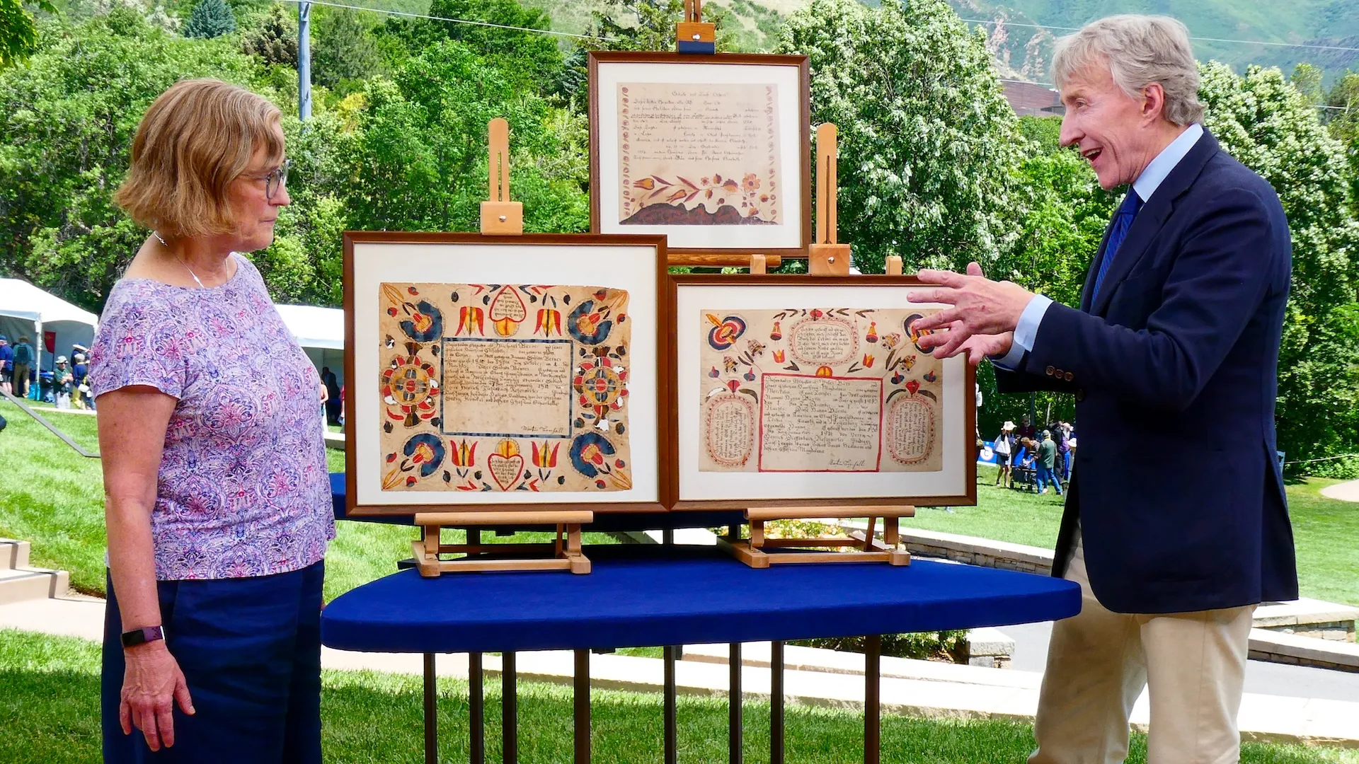Color photo of appraiser Leigh Keno discussing folk art with a woman outdoors with mountains in the background.